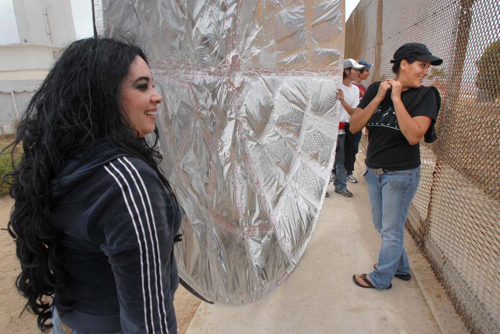 Jacqueline Torres, 23, right, listens to a person she is having a conversation with 150 feet away across the U.S.-Mexico border using a parabolic sound reflector. The organization Border Encuentro has begun to hold events using sound reflectors and sign language for people to communicate across the international border. Direct access to the border fence here has been stopped by the U.S. government. Photo - David Maung.