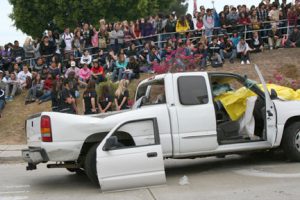 One of two crashed vehicles used in re-enacting drunk driving accident. Covered under the yellow tarp is “dead” Bonita Vista High student Carlos Valdivia. The school’s 11th and 12th graders look on from the front lawn of the school.