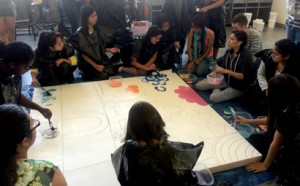 Inocente (right with the bowl of paint) is surrounded by a group of high school students from the university’s Upward Bound program