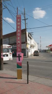 In 2015 the iconic pink and black crosses still stand in Juarez. This cross is painted on a pole for the 060 Emergency line. Coincidentally, a bus from the Number 10 line that passes by Sagrario’s house was parked nearby. Photo Credit: Bob Chessey